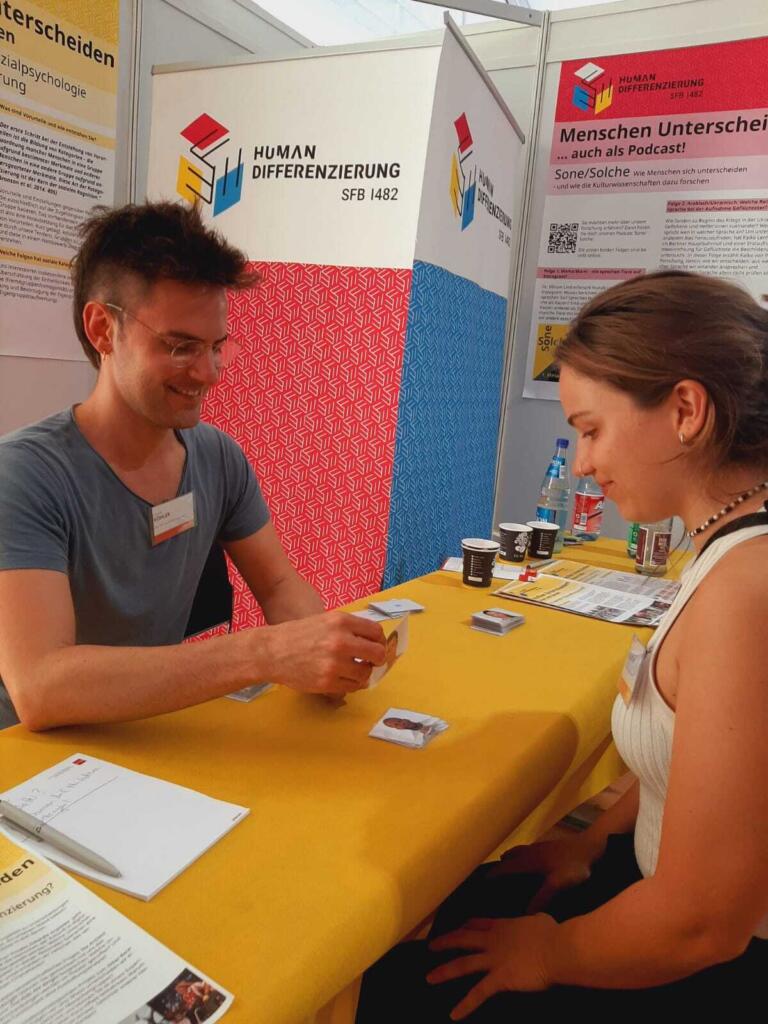 zwei Personen an einem Stand auf dem Mainzer Wissenschaftsmarkt führen ein Experiment zur Messung des Other-Race-Effects durch